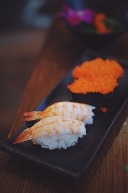 Close-up of shrimp nigiri sushi with vibrant tobiko on a black plate.