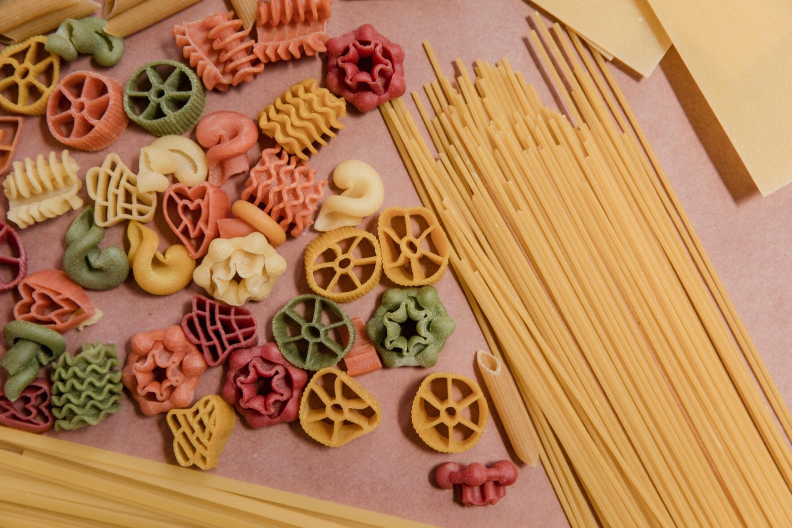 Top view of various colorful and textured raw pasta on a light surface.